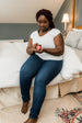 Woman sitting on a bed holding a small container, wearing a white shirt and blue jeans.